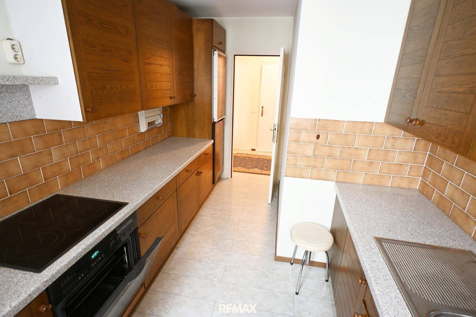Längliche Küche mit Holzschränken, Fliesen und integriertem Kühlschrank, gut ausgestattet.