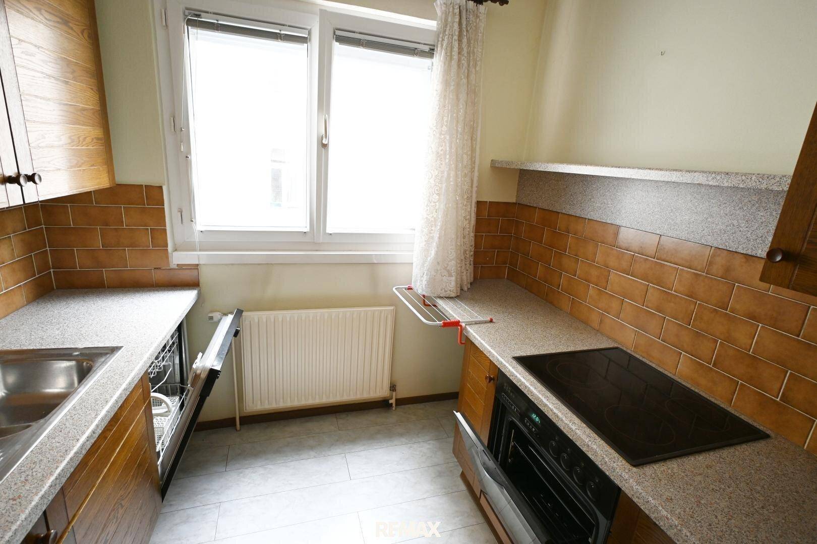 Küche mit Holzfronten, Arbeitsplatte und Fenster, bietet ausreichend Arbeitsfläche.