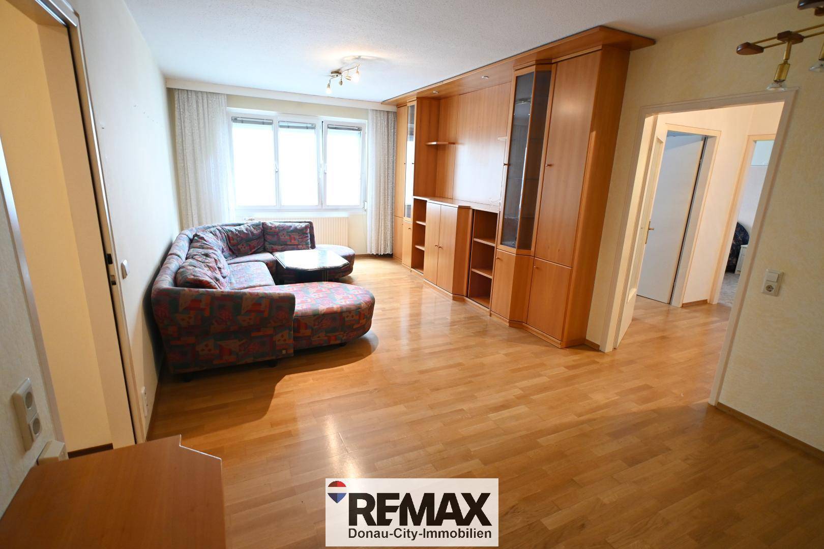 Gemütliches Wohnzimmer mit Parkettboden, Sofa und großer Schrankwand.