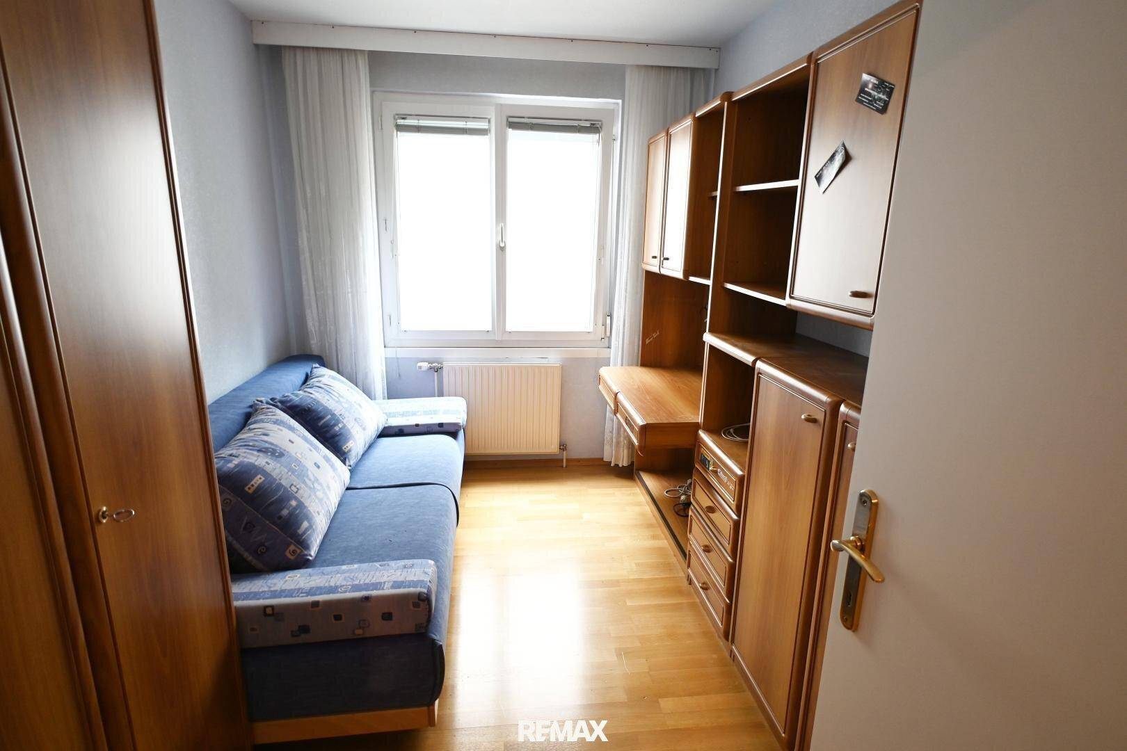 Kleines Zimmer mit Schlafsofa, Holzmöbeln und Parkettboden, funktional eingerichtet.