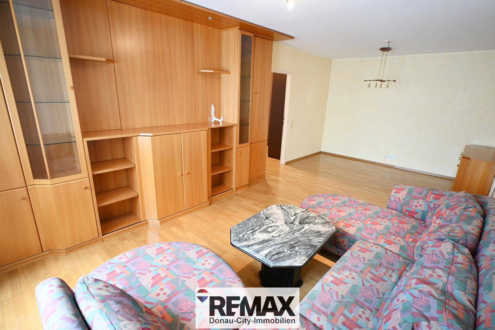 Wohnzimmer mit bequemer Sitzecke, Parkettboden und großer Holzschrankwand.