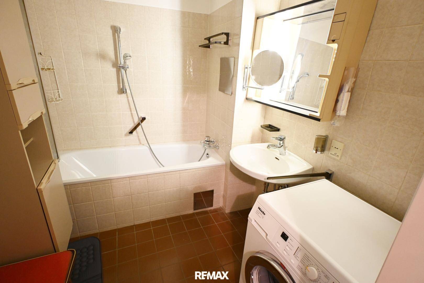 Badezimmer mit Badewanne, Waschbecken und Waschmaschine, hell gefliest und funktional.