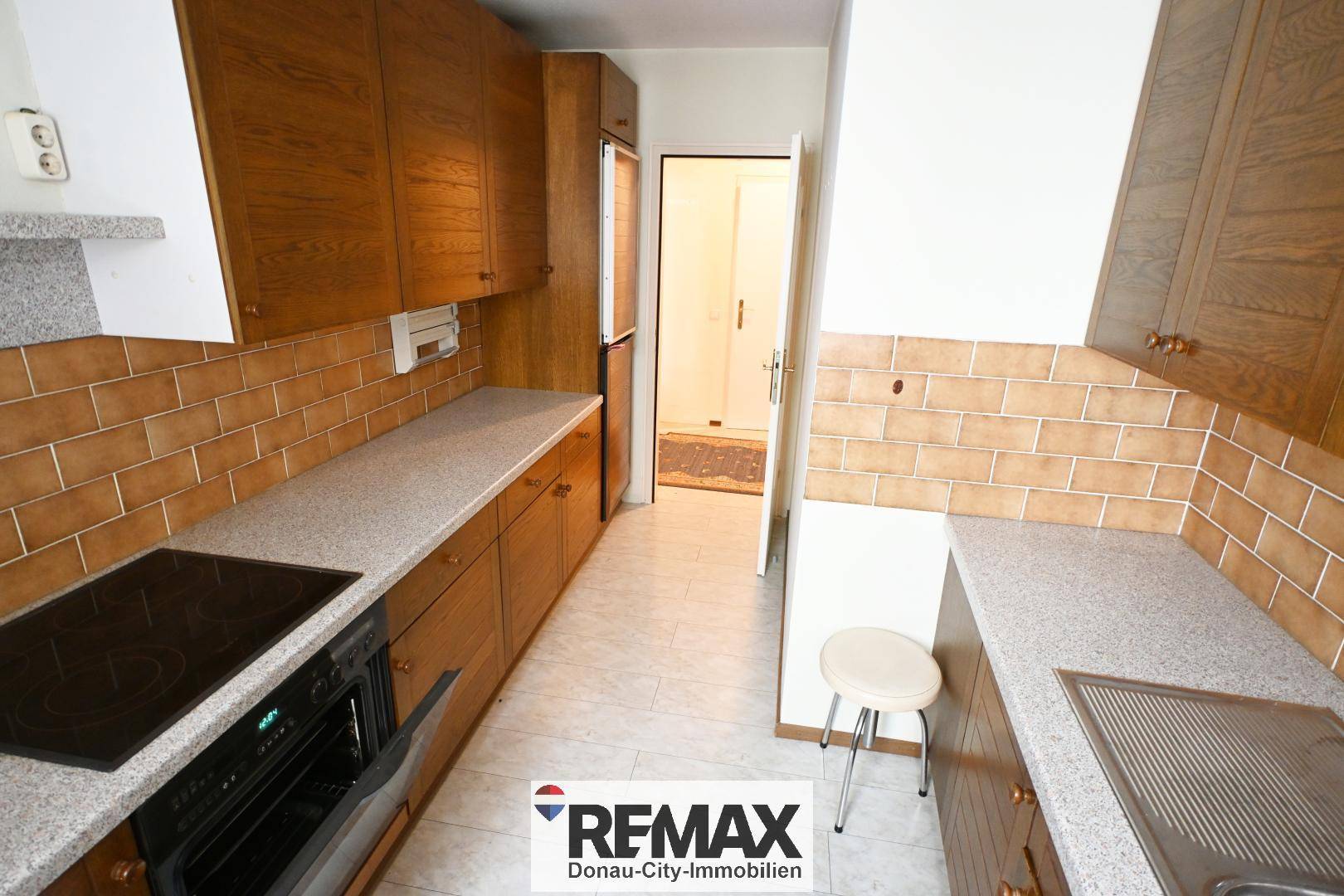 Längliche Küche mit Holzschränken, Fliesenboden und integriertem Kühlschrank.