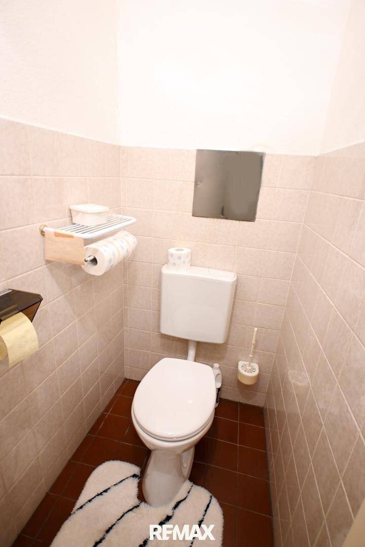Separate Toilette mit hellen Fliesen und kleinem Waschbecken, sauber und funktional.