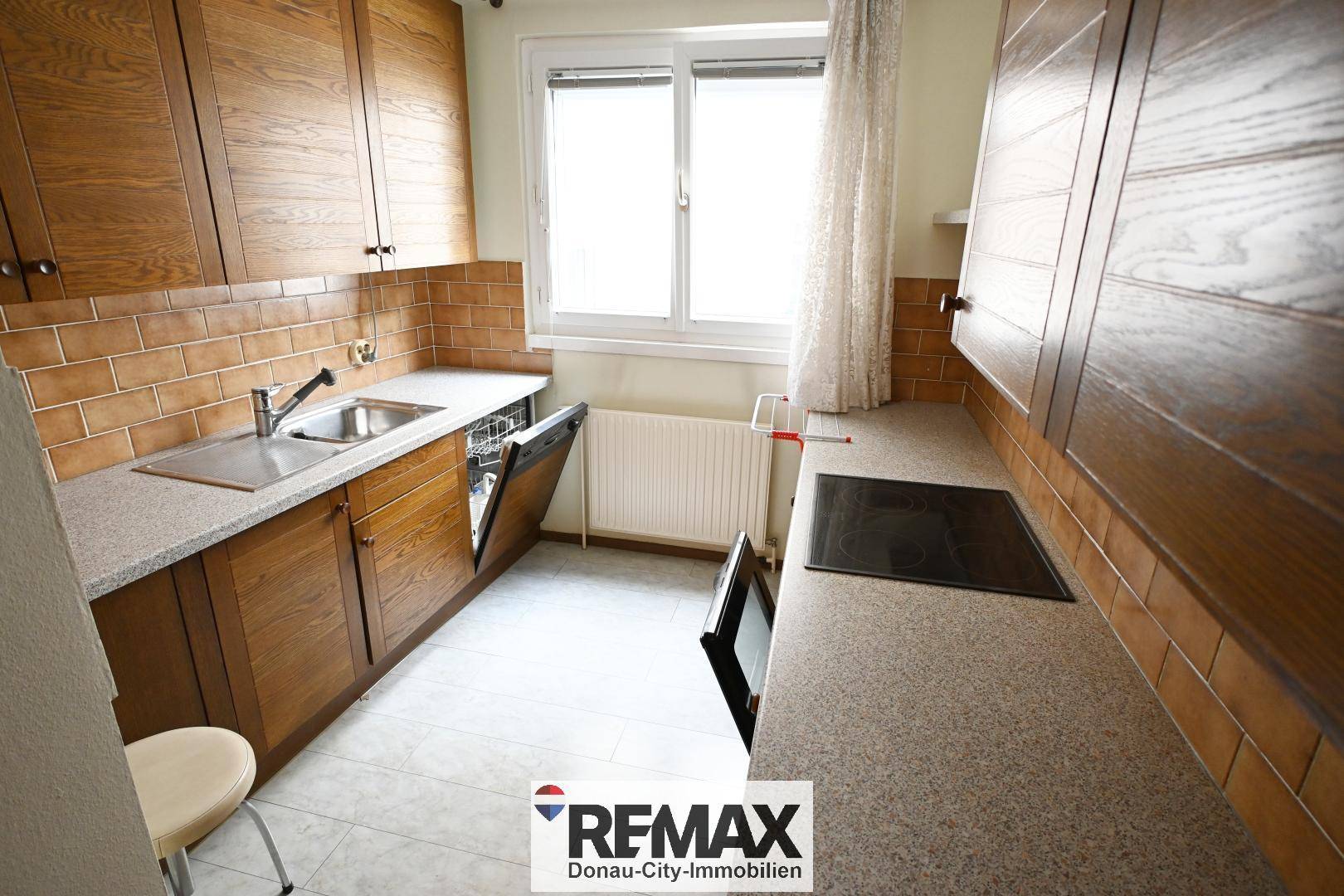 Funktionale Küche mit Holzschränken, Fliesenboden und Fenster, inklusive Geschirrspüler.