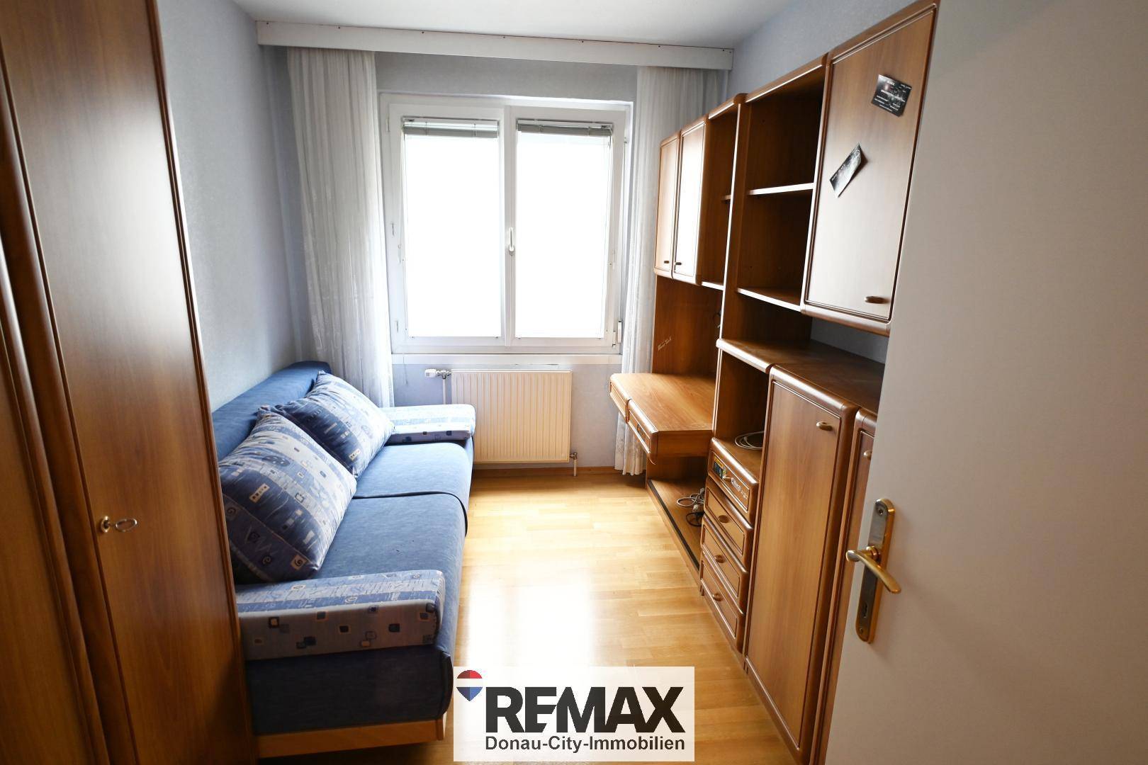 Kleines Zimmer mit Sofa, Holzmöbeln und Parkettboden, ideal als Gäste- oder Arbeitszimmer.