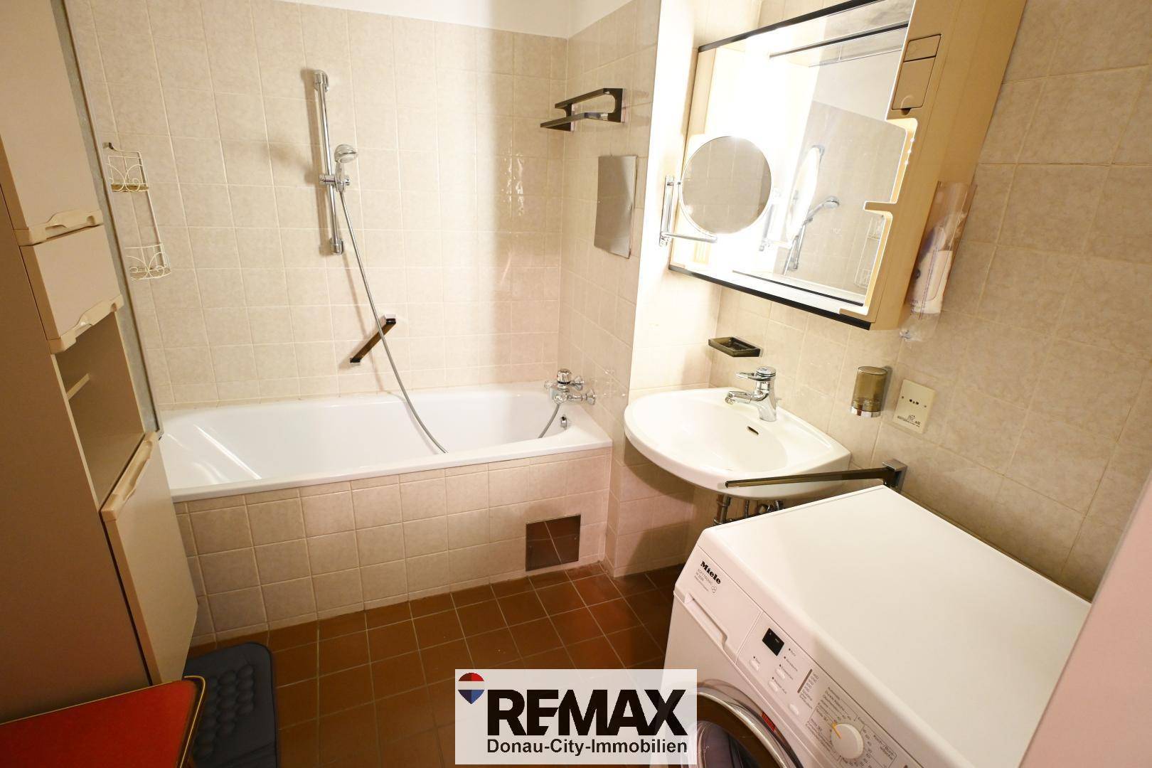 Badezimmer mit Badewanne, Waschbecken und Waschmaschine, hell gefliest.
