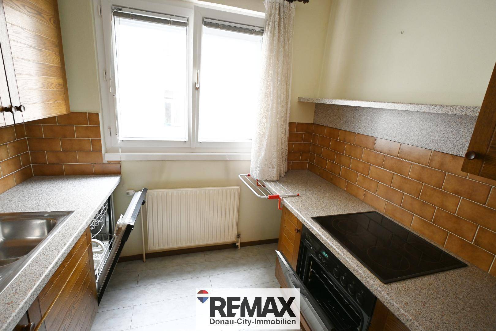 Küche mit braunen Holzfronten, Fliesenboden und Fenster, bietet Arbeitsfläche.