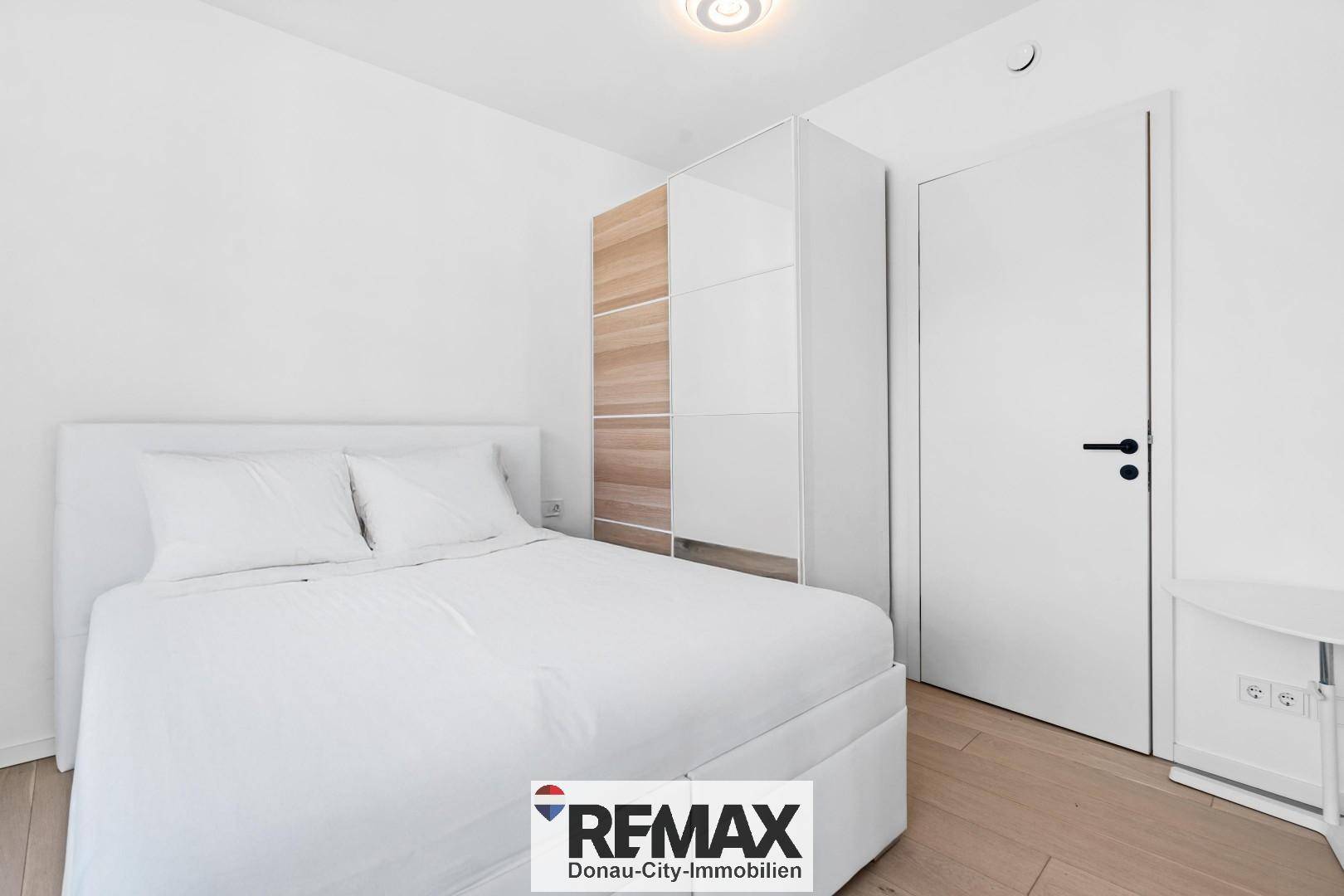 Modernes Schlafzimmer mit weißem Bett, Kleiderschrank und hellem Holzboden.