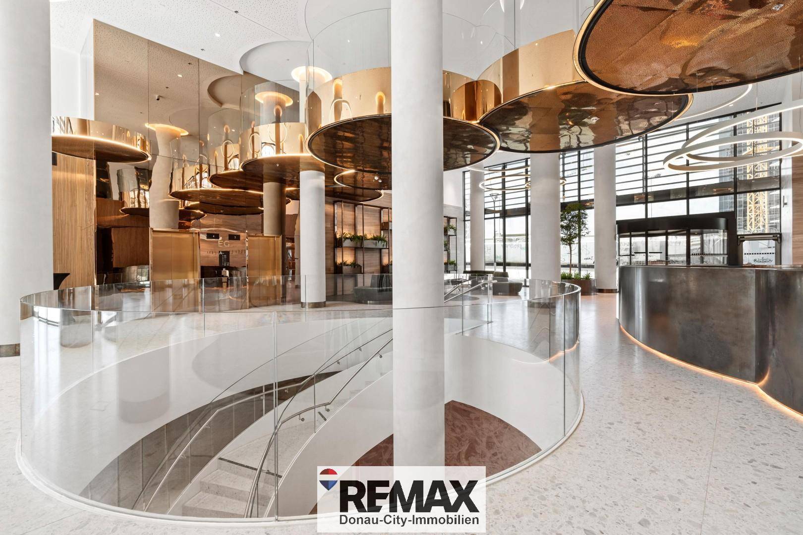 Elegante Lobby mit geschwungener Treppe, goldenen Deckenleuchten und modernen Säulen.