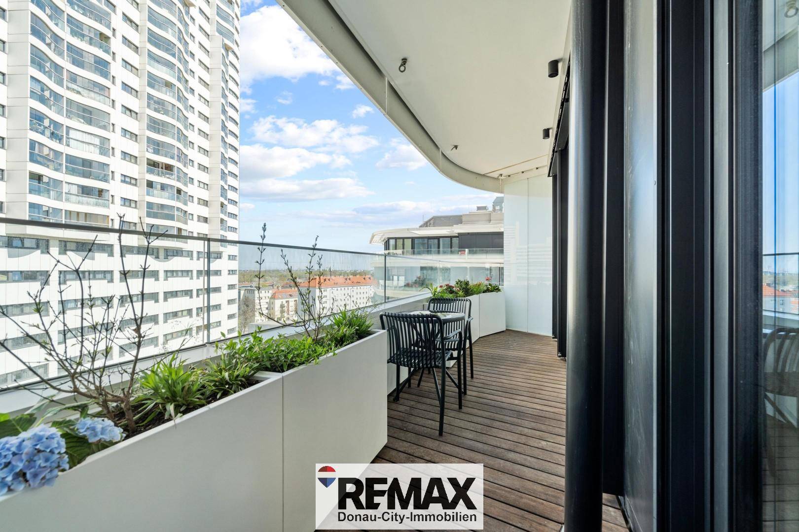 Langer Balkon mit Holzboden, Blumenkästen und moderner Glasbrüstung.