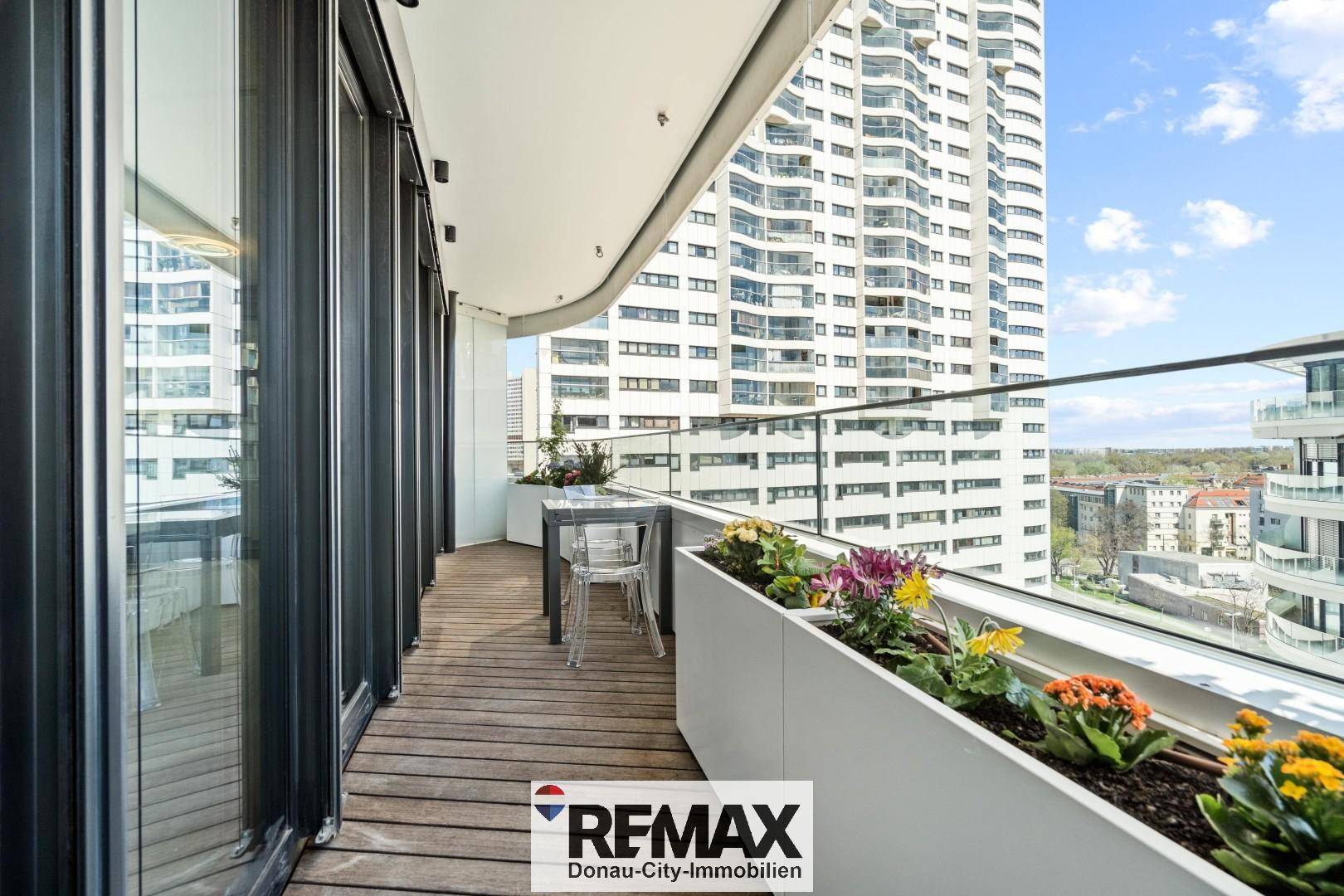 Geräumiger Balkon mit Holzboden, Glasbrüstung und Blick auf die Stadt.