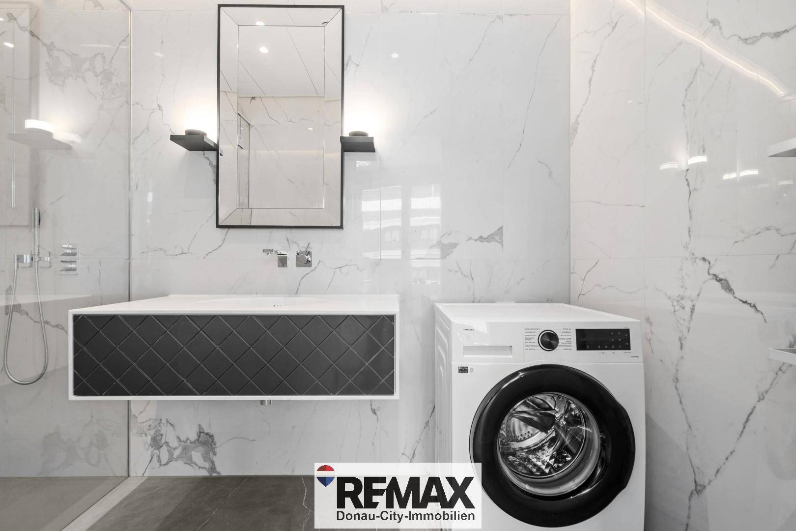 Modernes Badezimmer mit Marmorfliesen, Waschbecken und Waschmaschine.