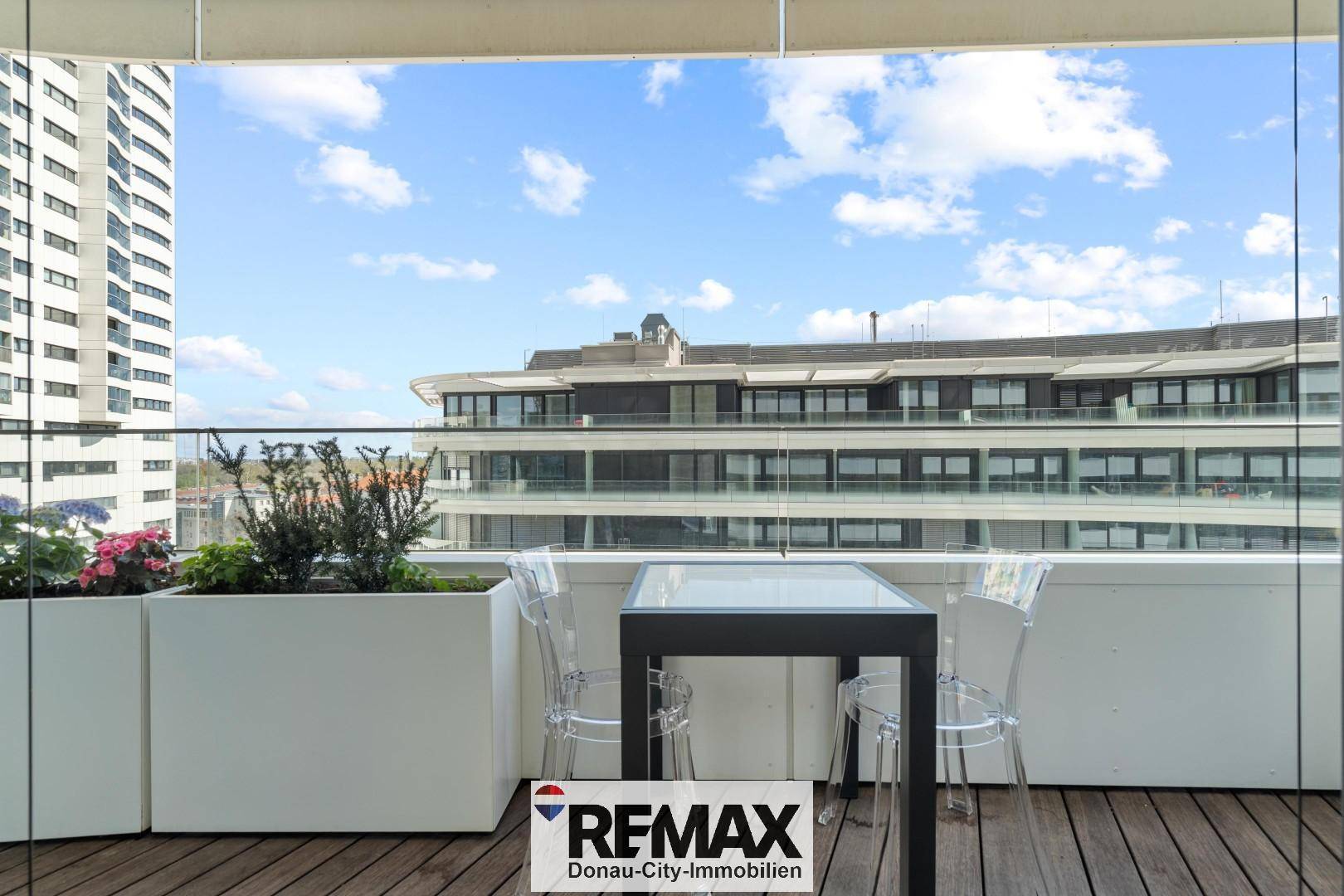 Heller Balkon mit Tisch und Stühlen, umgeben von modernen Gebäuden.