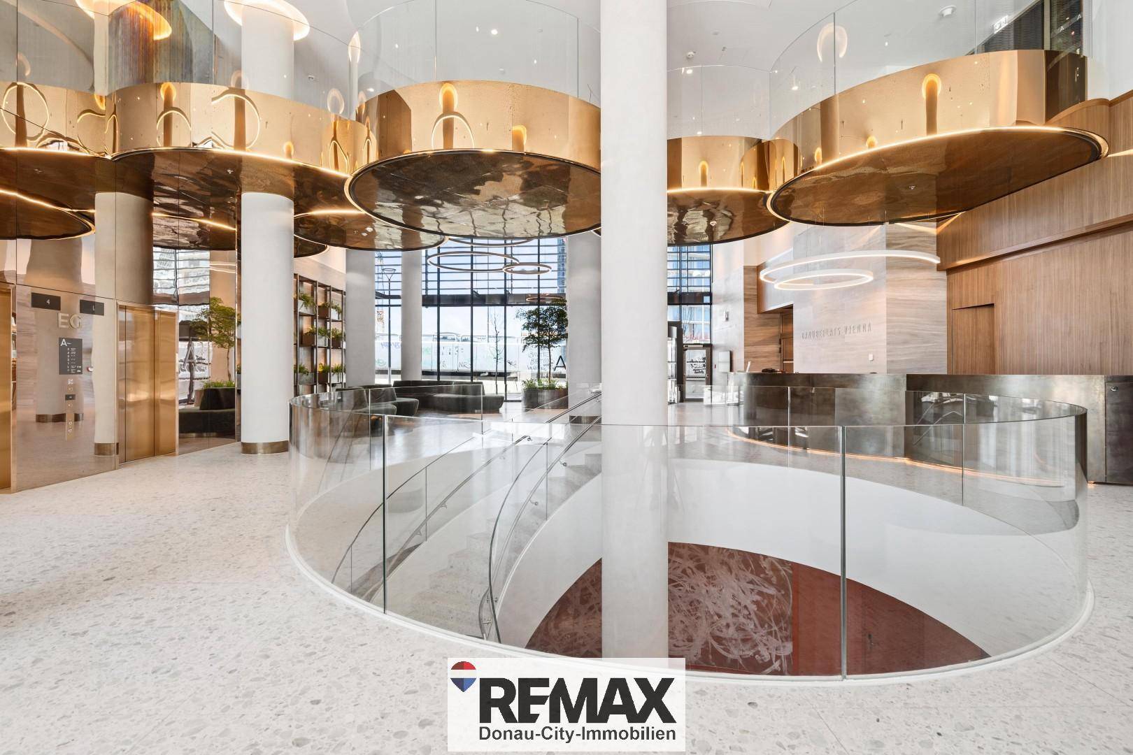 Luxuriöse Lobby mit geschwungener Treppe, goldenen Akzenten und viel Tageslicht.