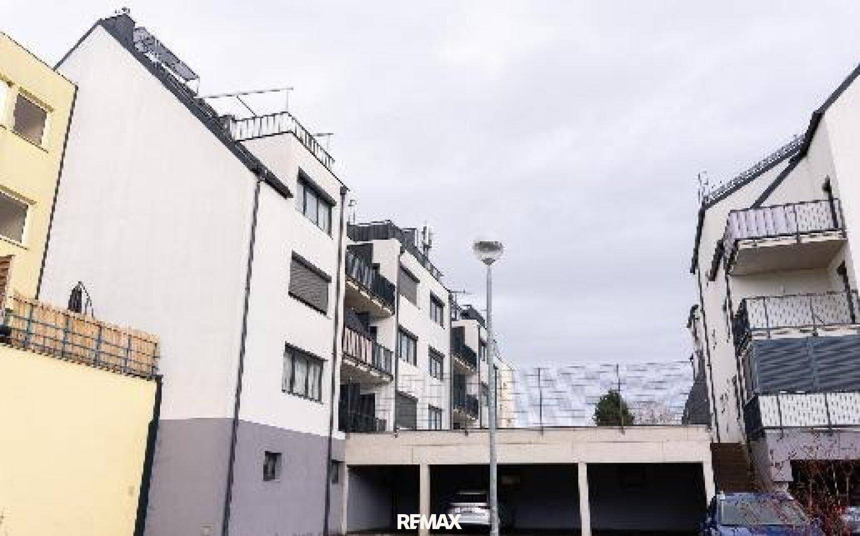 Seitenansicht des Wohnkomplexes mit Tiefgaragenzufahrt und Balkonen unter bewölktem Himmel.