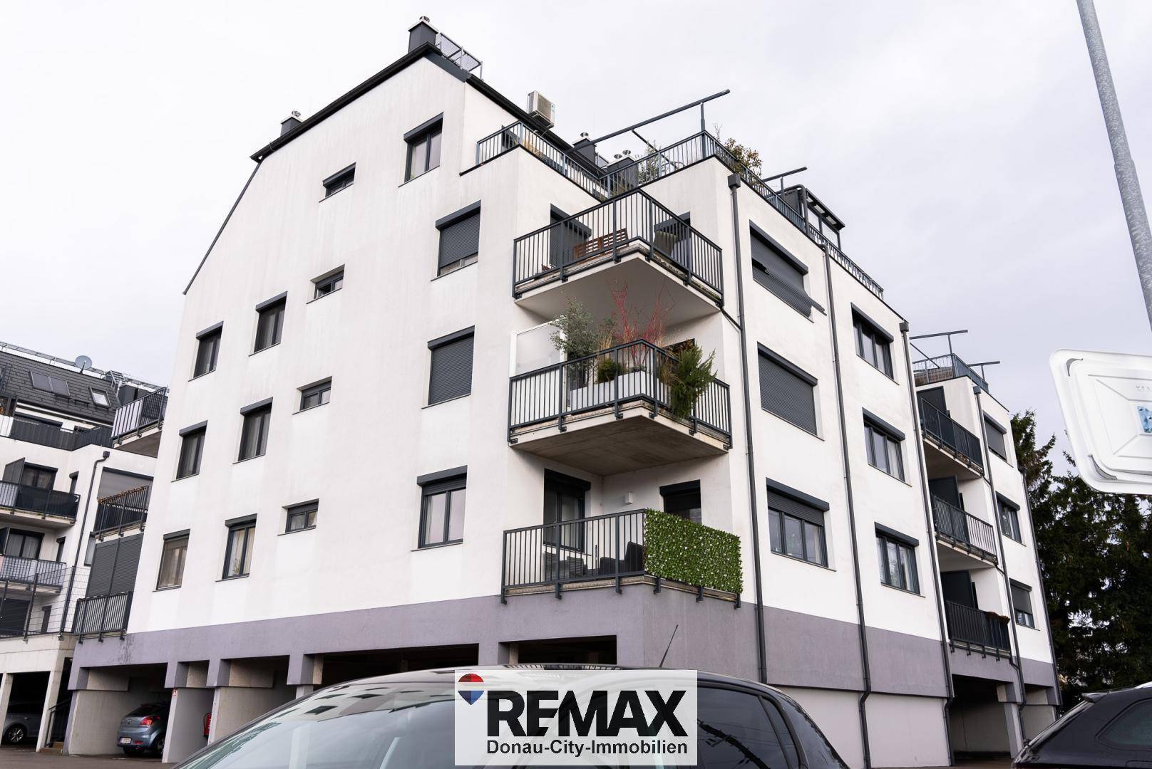 Ansicht eines modernen Mehrfamilienhauses mit Balkonen und dunklen Fensterläden.