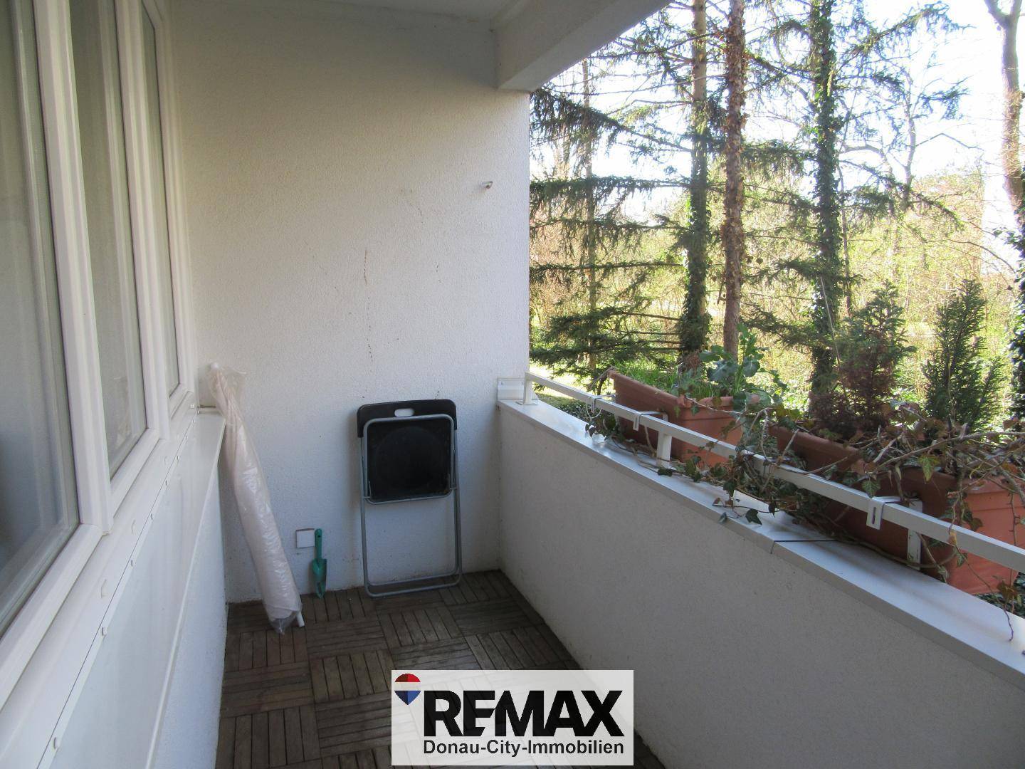 Kleiner Balkon mit Holzbodenfliesen, einem Klappstuhl und Blick ins Grüne.