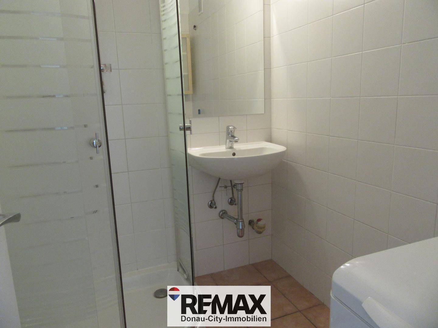 Modernes Badezimmer mit weißen Fliesen, Duschkabine und Einzelwaschbecken.