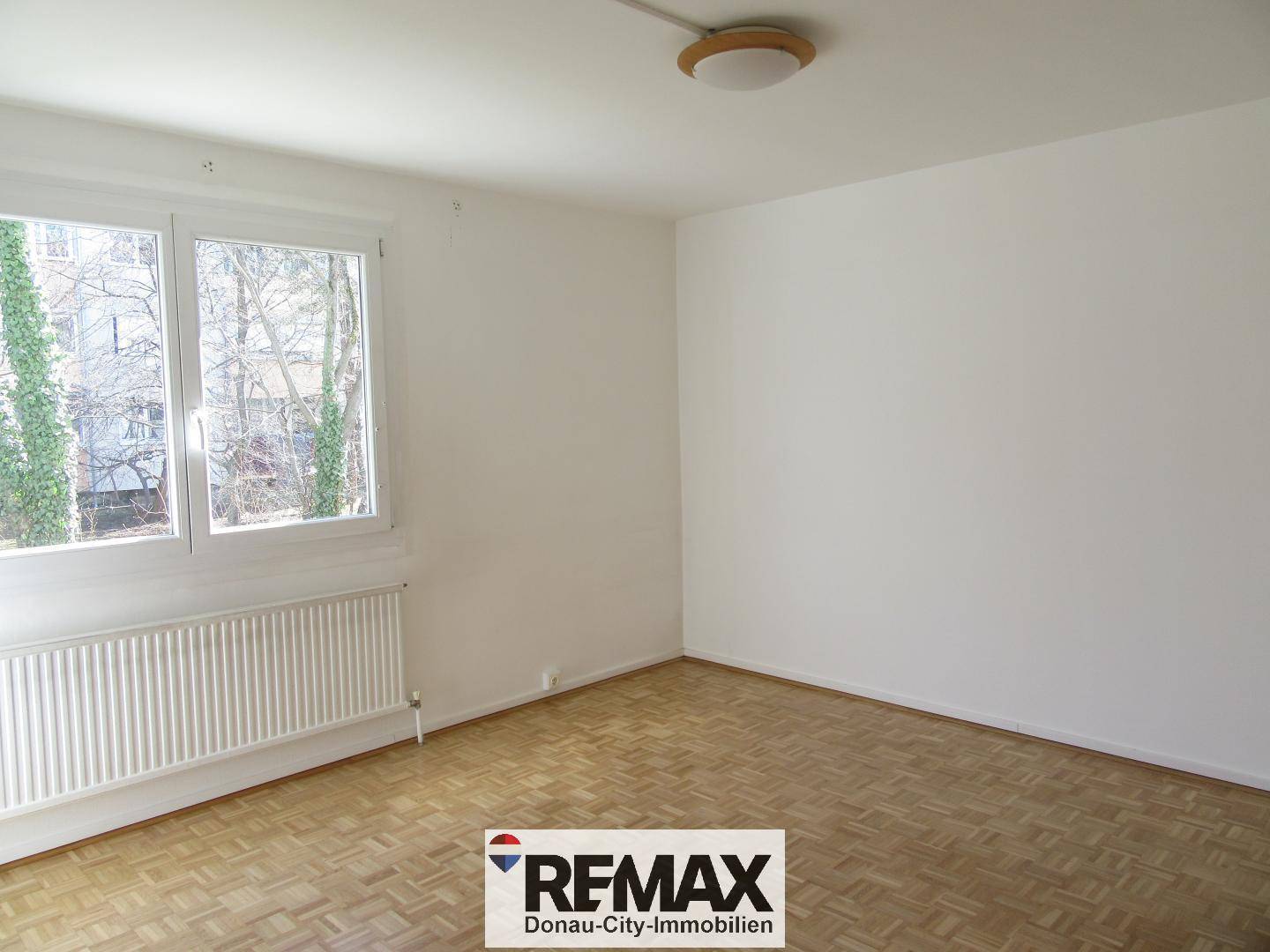 Helles Schlafzimmer mit Parkettboden, weißen Wänden und großem Fenster.