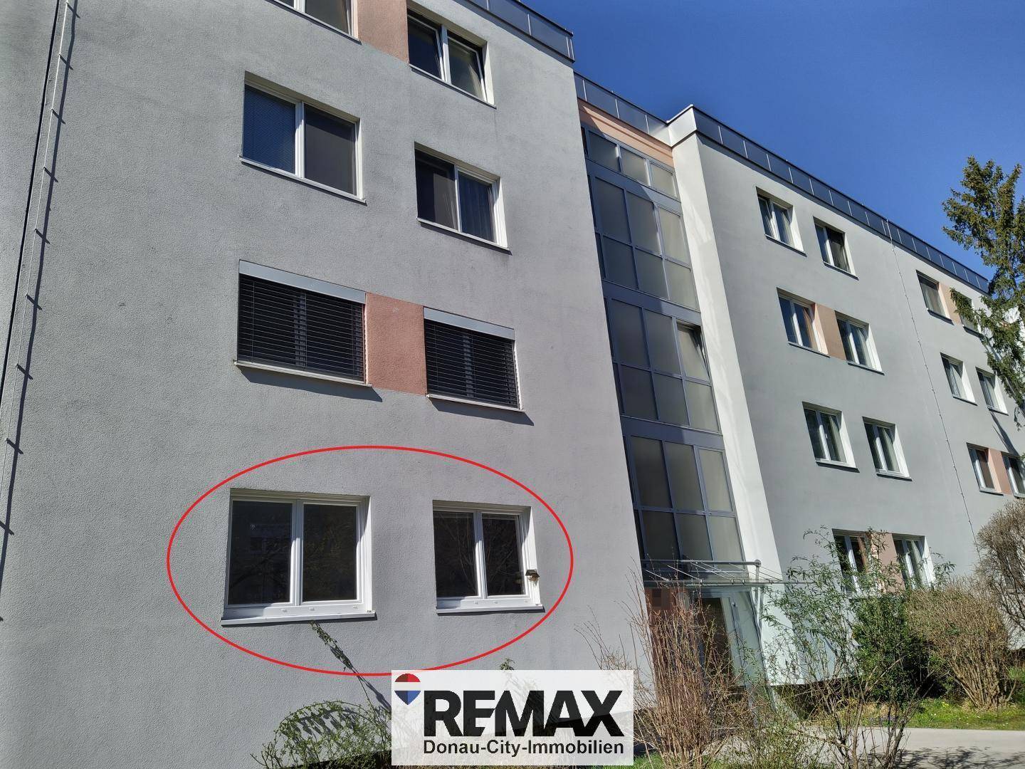 Fassade eines Mehrfamilienhauses mit großen Fenstern und einem verglasten Aufzugsschacht.