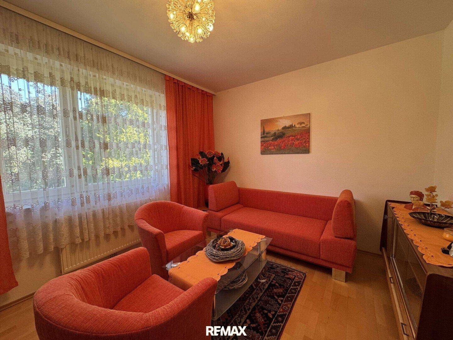 Helles Wohnzimmer mit orangefarbenen Sofas, Parkettboden und großen Fenstern.