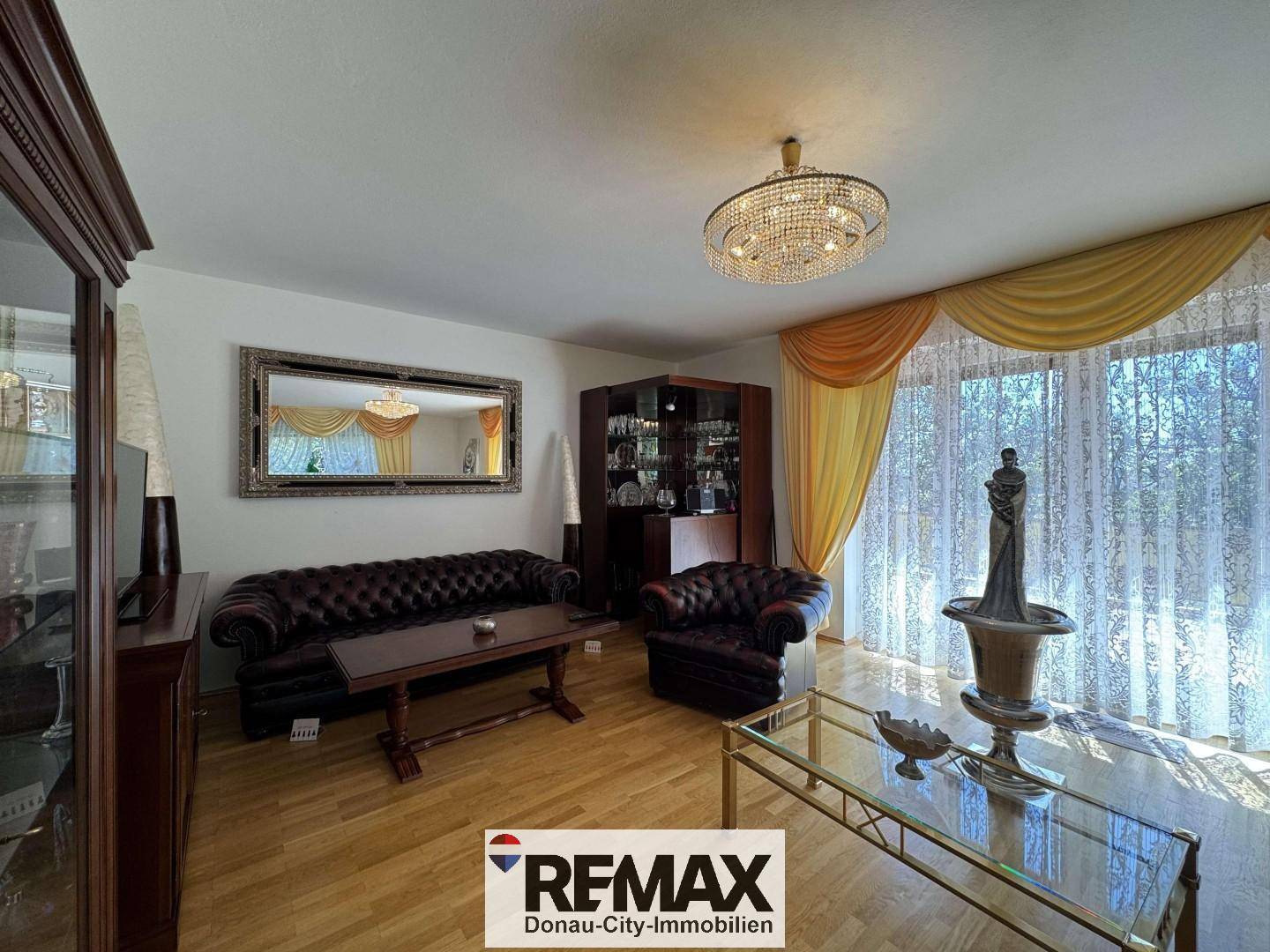 Geräumiges Wohnzimmer mit Ledersofas, Holzboden und großen Fenstern mit gelben Vorhängen.