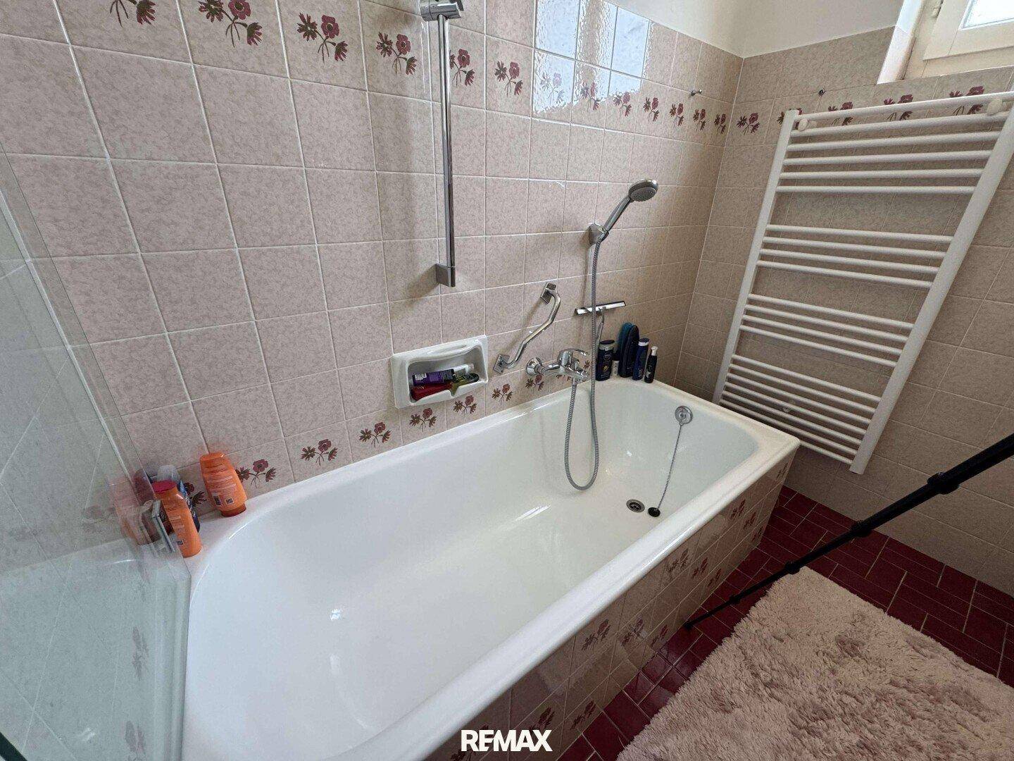 Badezimmer mit Badewanne, Fliesenboden und beheiztem Handtuchhalter.