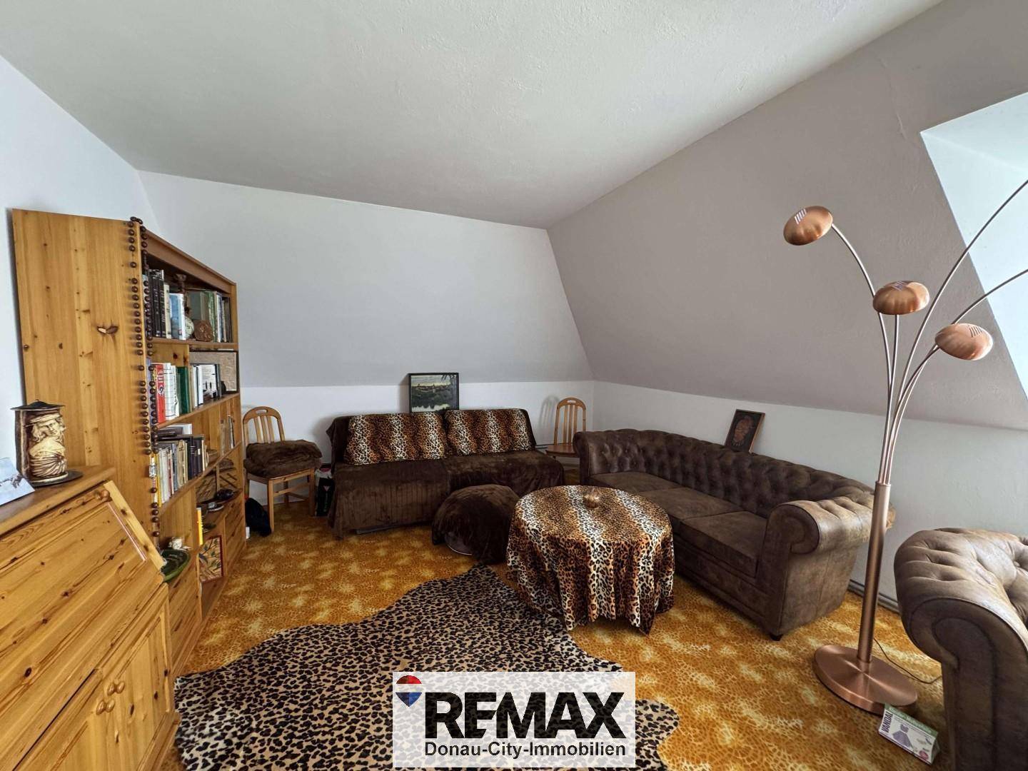 Wohnzimmer im Dachgeschoss mit schräger Decke, braunen Sofas und auffälligem Leopardenmuster-Teppich.