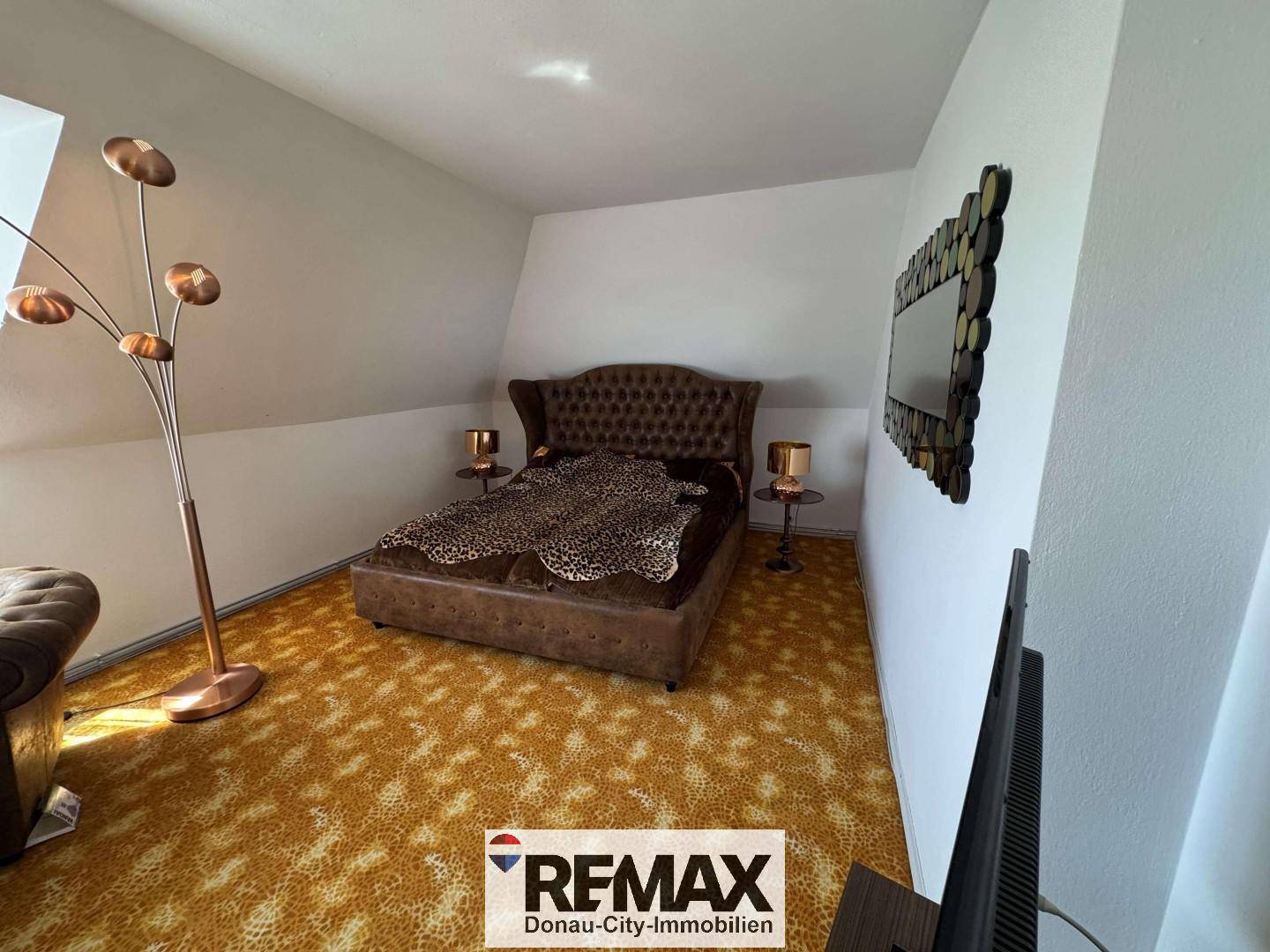 Schlafzimmer im Dachgeschoss mit schräger Decke, großem Bett und modernem Stehlampen-Design.