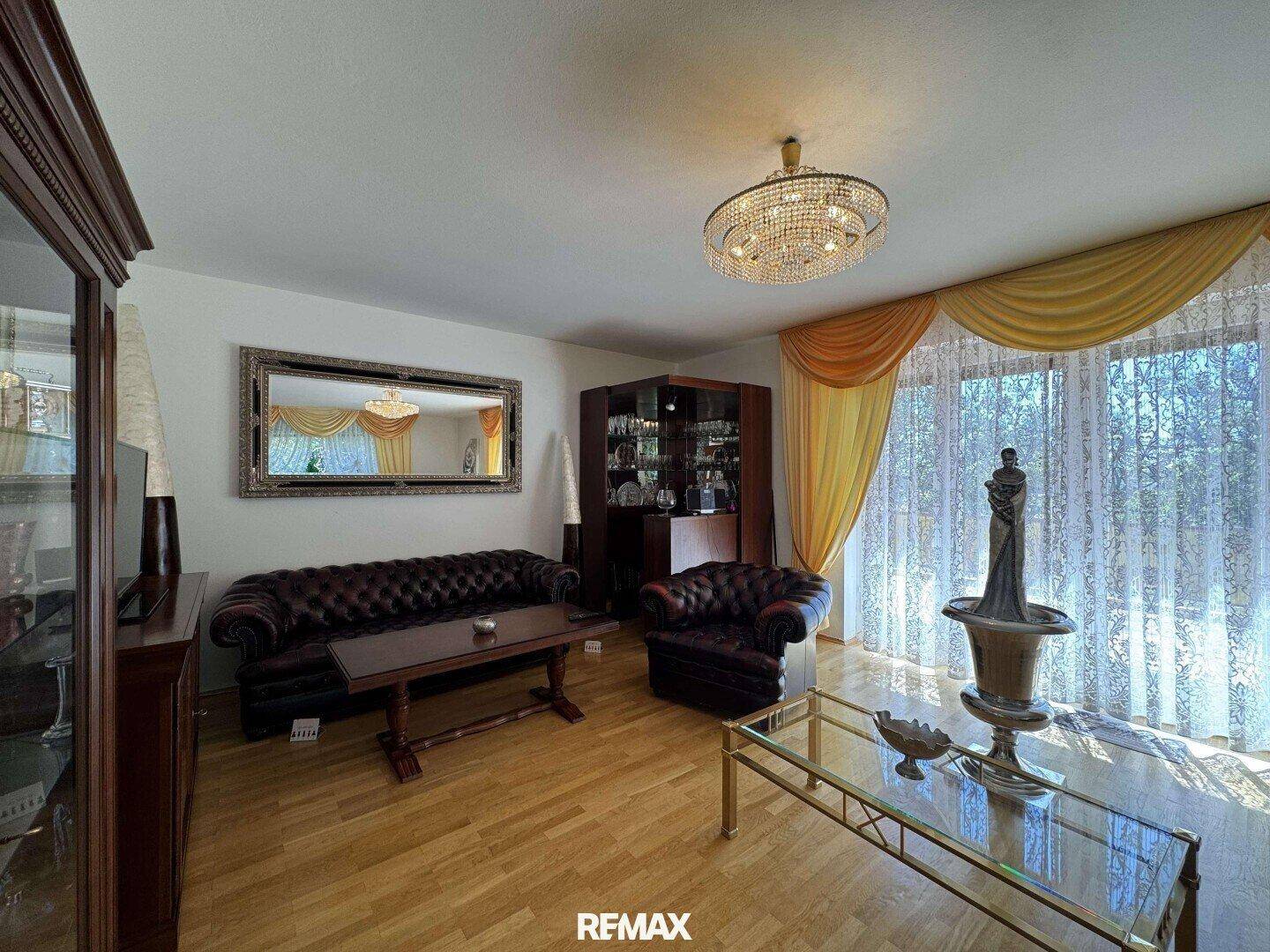 Geräumiges Wohnzimmer mit Parkettboden, Ledersofas und einem Kronleuchter.