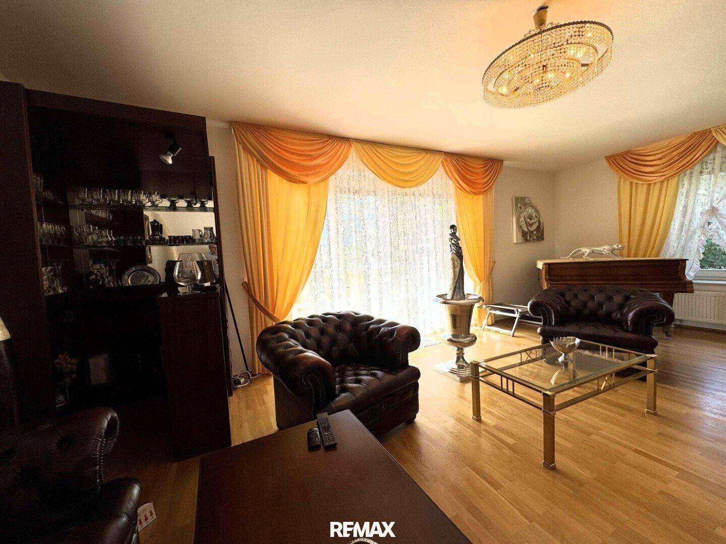 Helles Wohnzimmer mit Parkettboden, Ledersesseln und einem eleganten Kronleuchter.