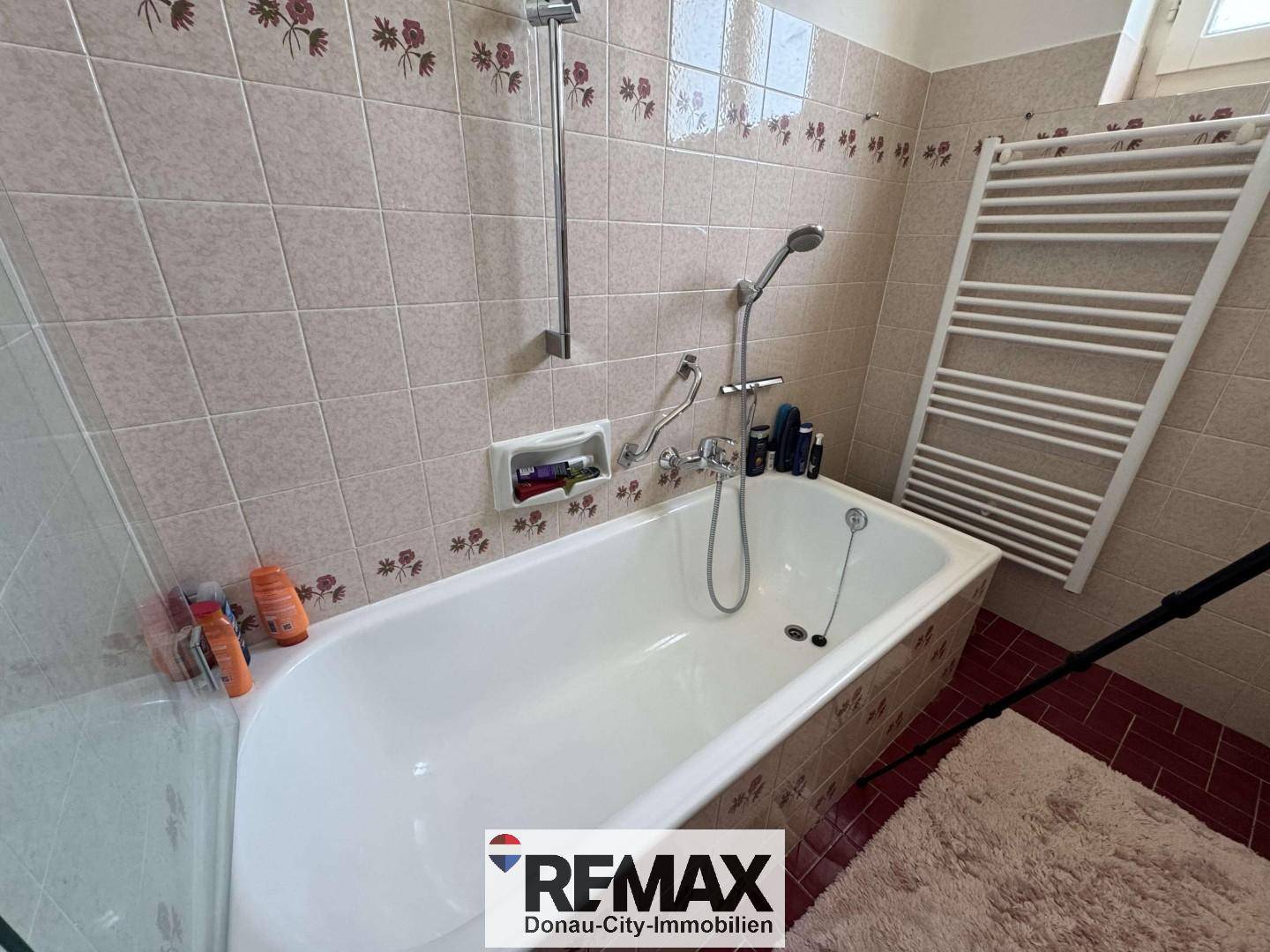 Badezimmer mit Badewanne, beigefarbenen Fliesen und beheiztem Handtuchhalter.