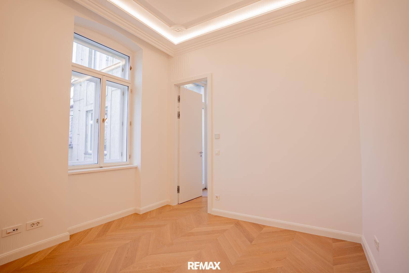 Helles Zimmer mit Fischgrätparkett und einem großen Fenster, ideal als Schlaf- oder Arbeitszimmer.