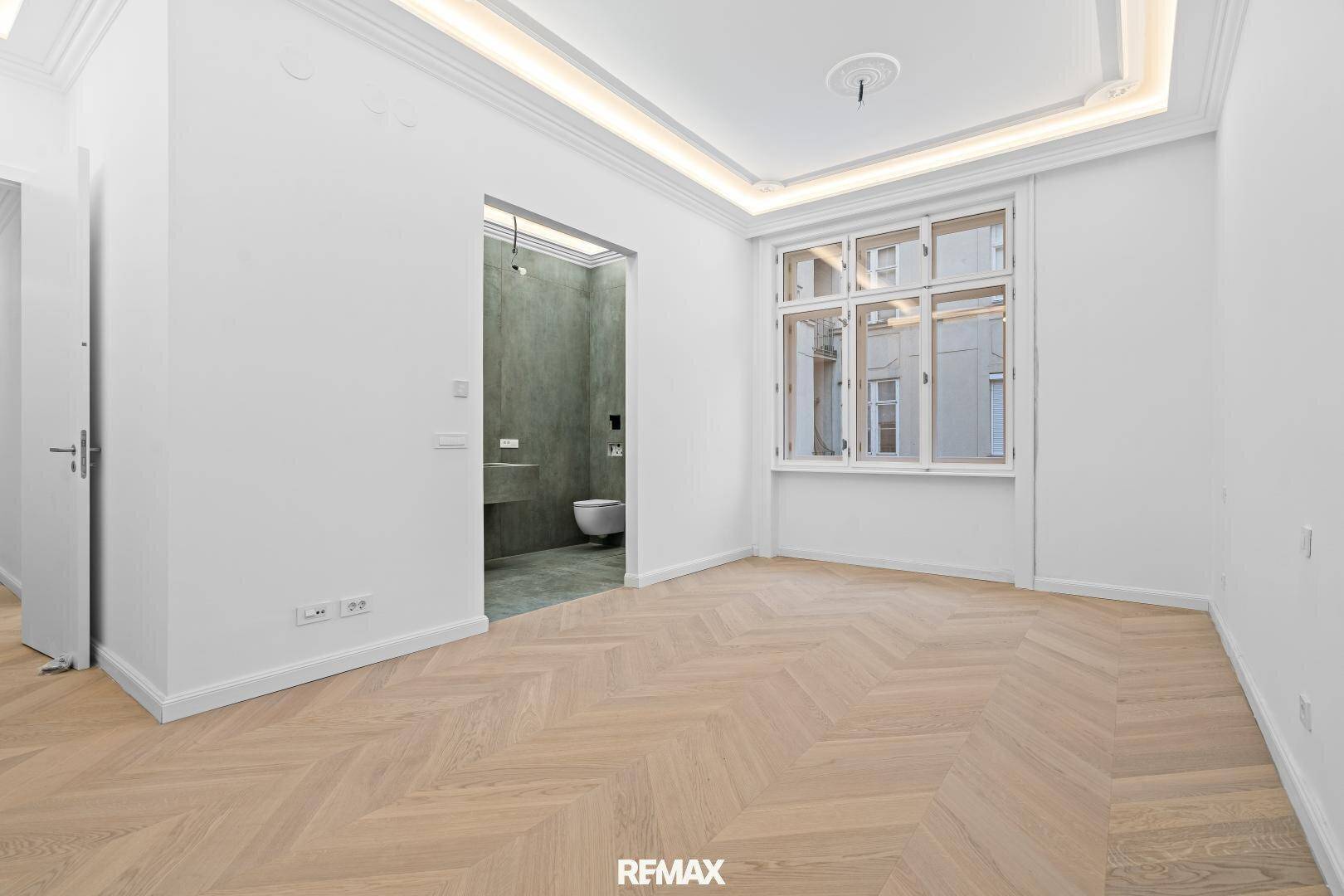 Geräumiges Zimmer mit Fischgrätparkett und Zugang zu einem modernen Badezimmer.