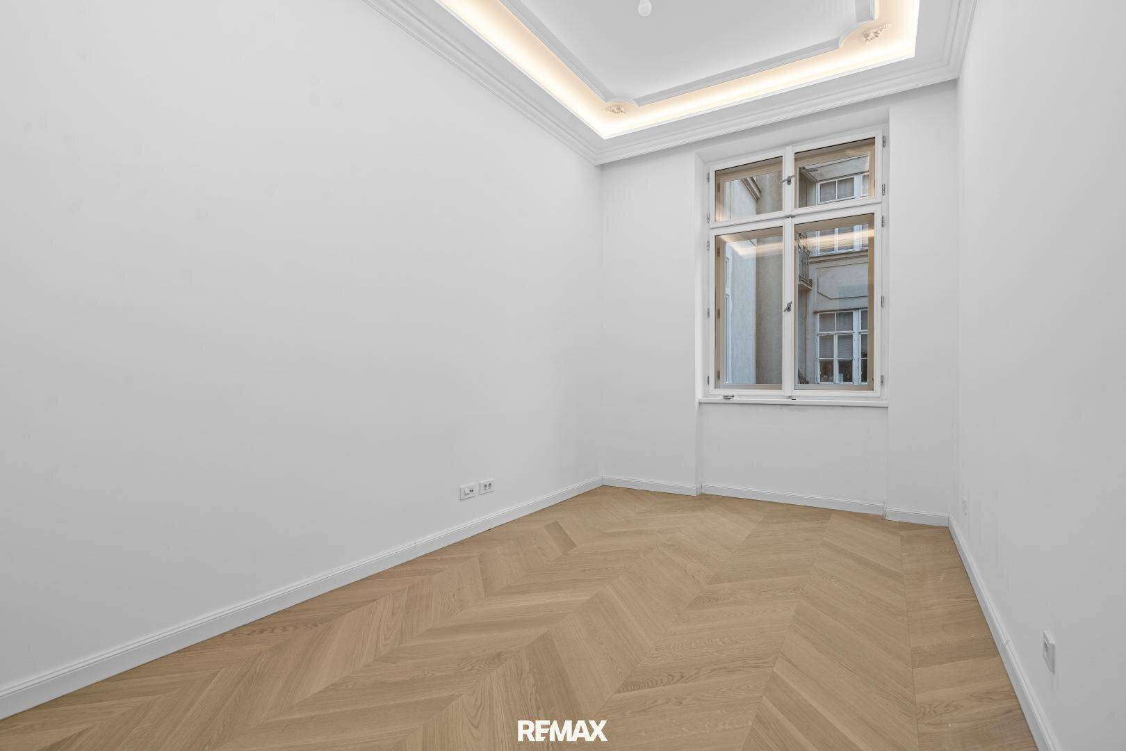 Ruhiges Zimmer mit Fischgrätparkett und einem großen Fenster, ideal für Schlaf- oder Arbeitszwecke.