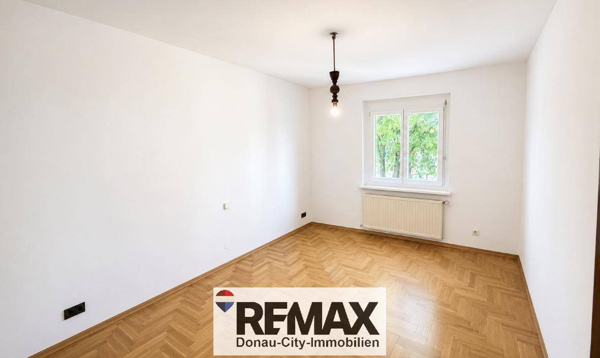 Geräumiges Zimmer mit Fischgrätparkett, weißen Wänden und einem Fenster, das viel Tageslicht bietet.