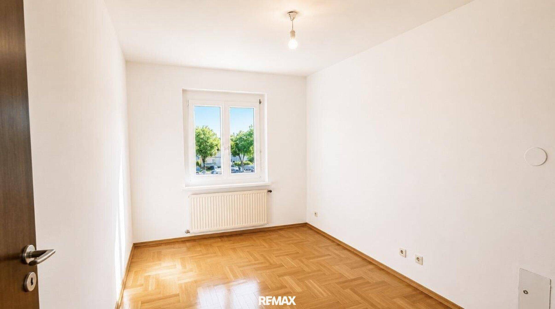 Ruhiges Schlafzimmer mit hellem Fischgrätparkett, weiß gestrichenen Wänden und Fenster.