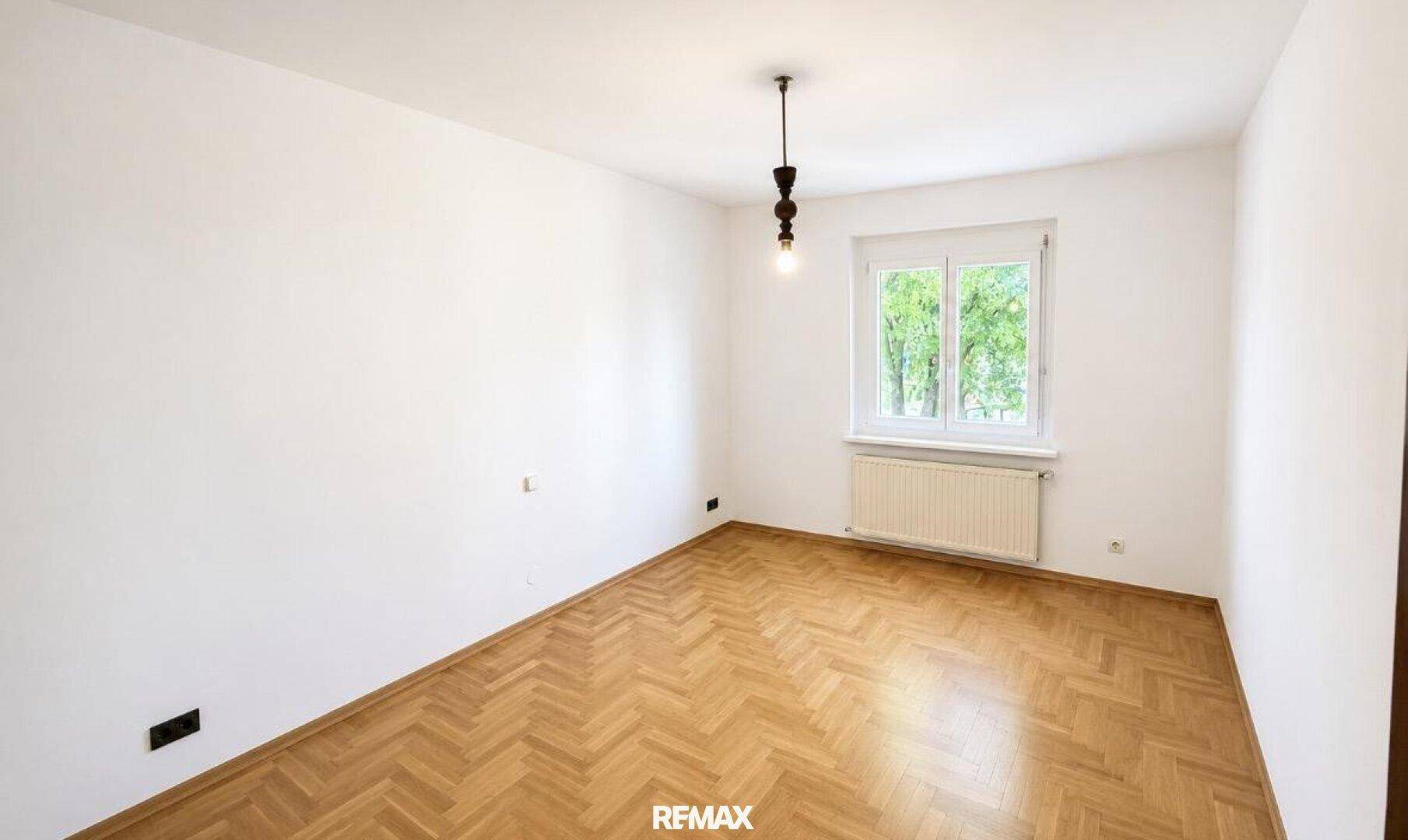 Geräumiges Schlafzimmer mit Fischgrätparkettboden, weißen Wänden und natürlichem Lichteinfall.