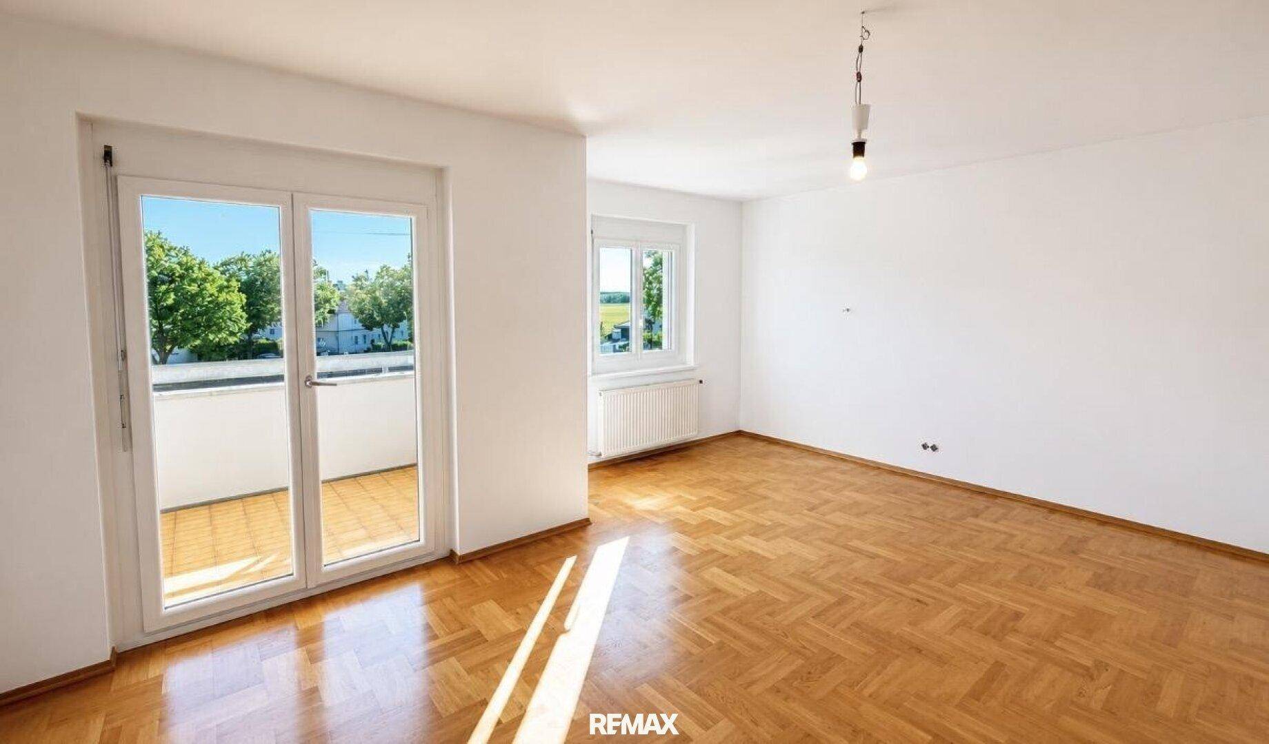 Geräumiges Wohnzimmer mit hellem Fischgrätparkett und direktem Zugang zum sonnigen Balkon.
