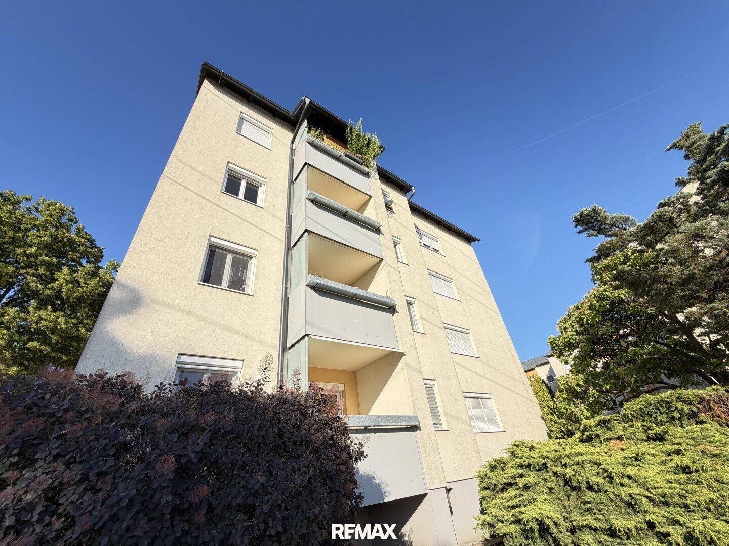 Mehrstöckiges Wohngebäude mit mehreren Balkonen und einer hellen Fassade unter blauem Himmel.