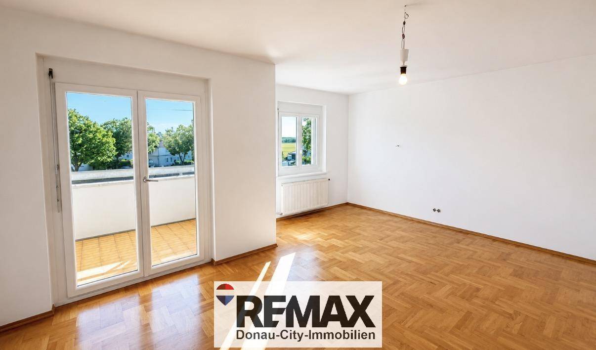 Geräumiges Wohnzimmer mit Fischgrätparkett, Zugang zum Balkon und weitem Blick durch das Fenster.
