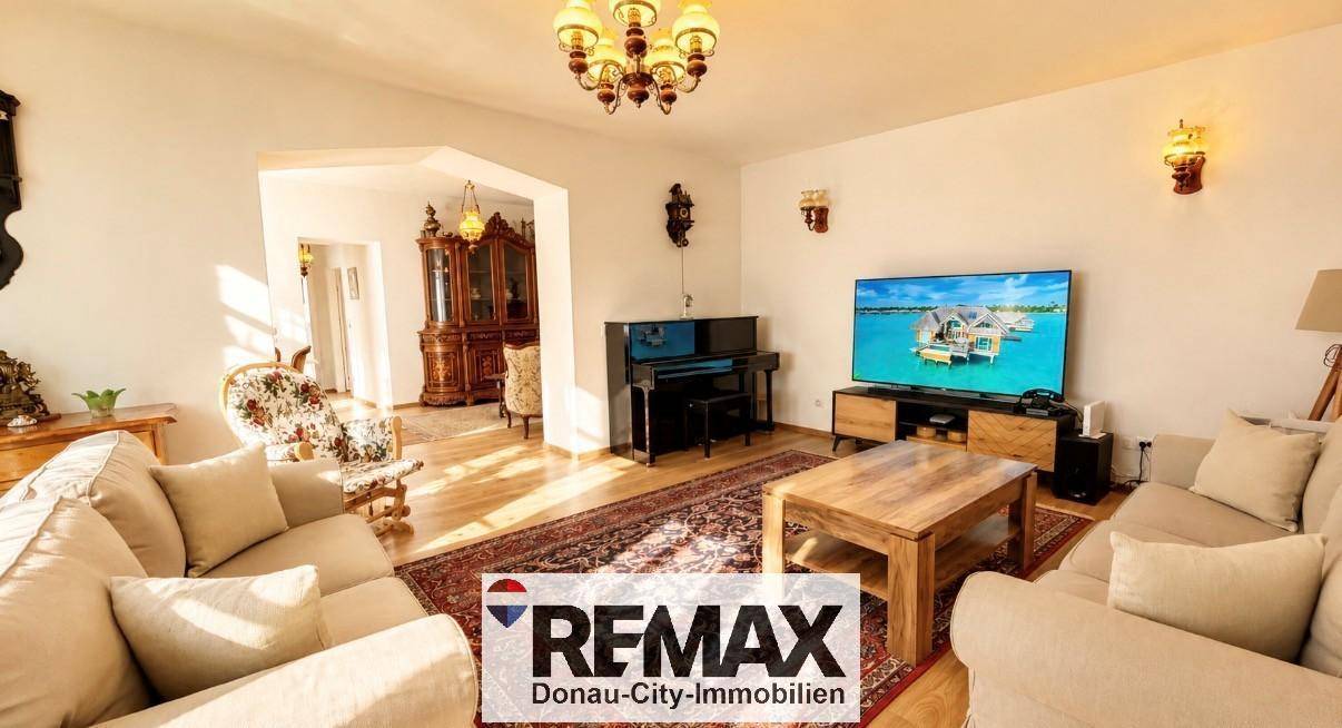 Gemütliches Wohnzimmer mit beigen Sofas, Holztisch, Fernseher und traditionellen Möbeln.