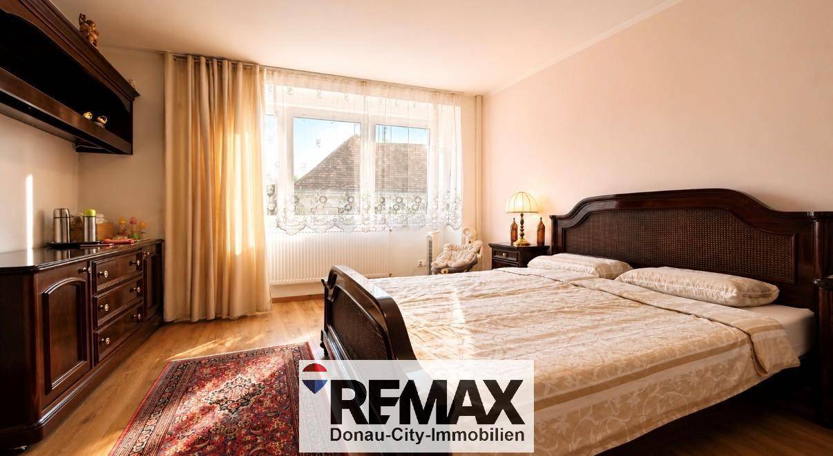 Helles Schlafzimmer mit großem Doppelbett, dunklen Holzmöbeln und Vorhängen am Fenster.