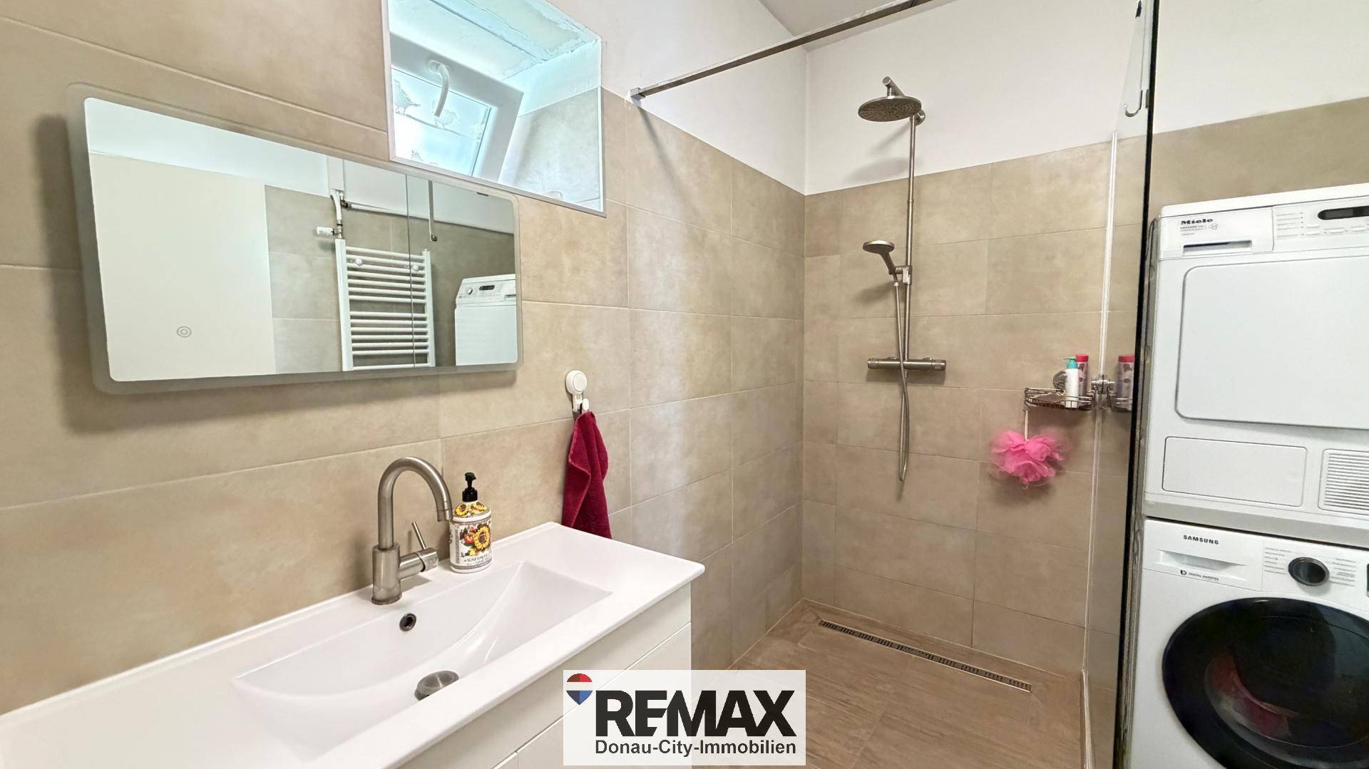 Modernes Badezimmer mit ebenerdiger Dusche, Waschbecken und gestapelter Waschmaschine und Trockner.