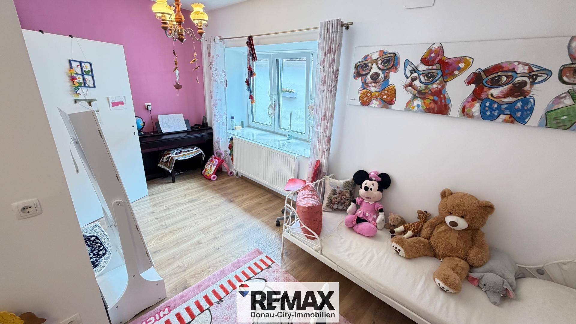 Kinderzimmer mit Bett, Spielzeug, bunten Bildern und rosa Wänden.
