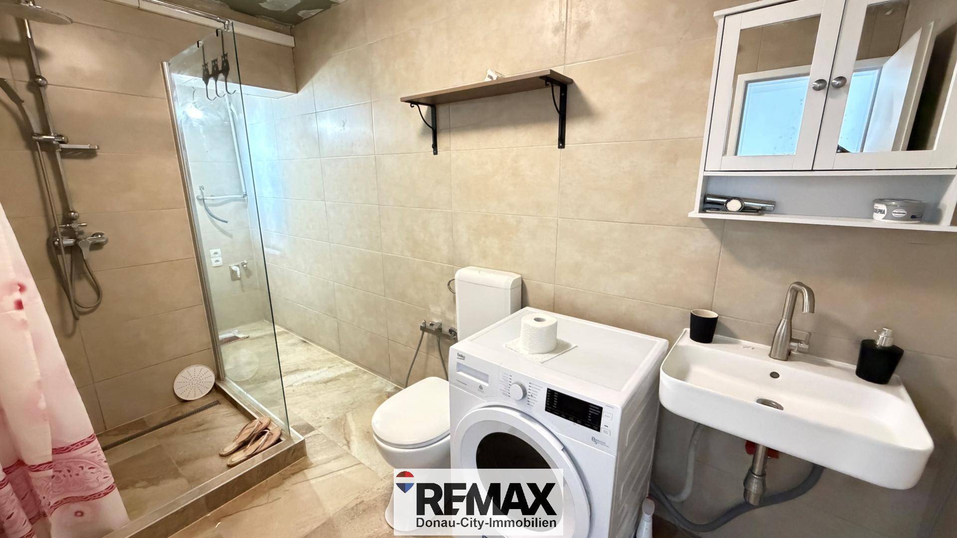 Funktionales Badezimmer mit Dusche, Waschbecken, Toilette und einer Waschmaschine.