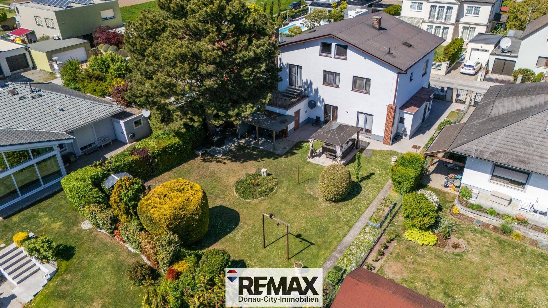 Rückansicht des Hauses mit großem Garten, überdachtem Sitzbereich und weiteren Häusern in der Umgebung.