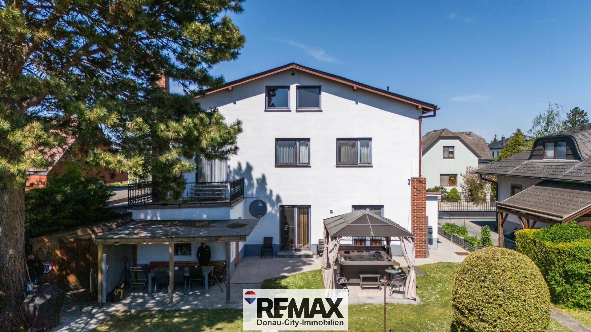 Rückseite des Hauses mit großer Terrasse, überdachtem Sitzbereich und Blick in den Garten.