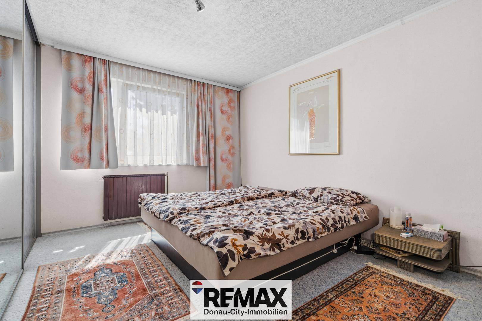 Schlafzimmer mit Doppelbett, Teppichboden und einem Fenster mit gemusterten Vorhängen.